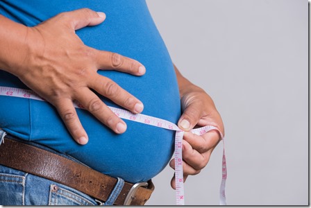 Overweight or fat adult man in very tight jeans with measuring tape on a gray background. Healthcare, medicine concept.