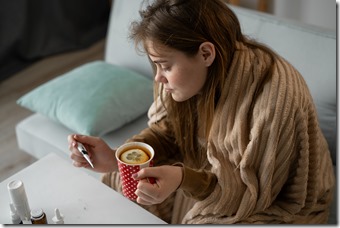 sick woman takes her temperature and drinks tea with lemon for cold. viral infection