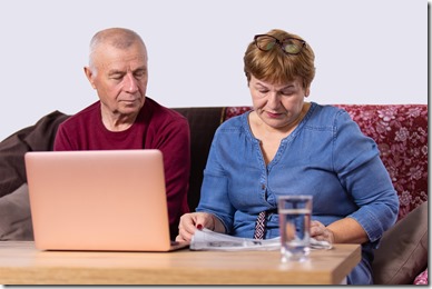 Aged couple going about their business, woman reading a newspaper and man opened laptop and sitting near his wife. High quality photo