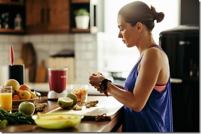 Athletic woman slicing fruit while preparing smoothie in the kitchen. 